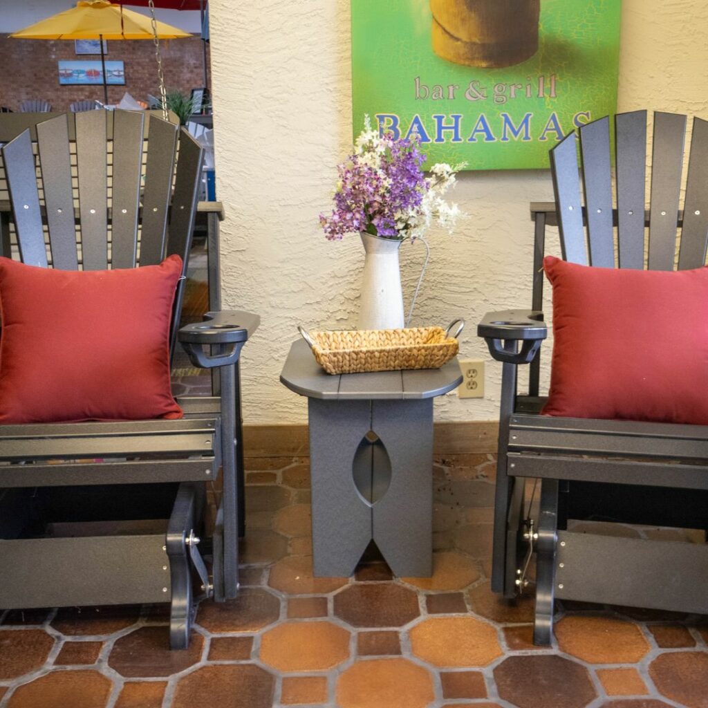 two brown gliding chairs with red pillows and a table in-between them